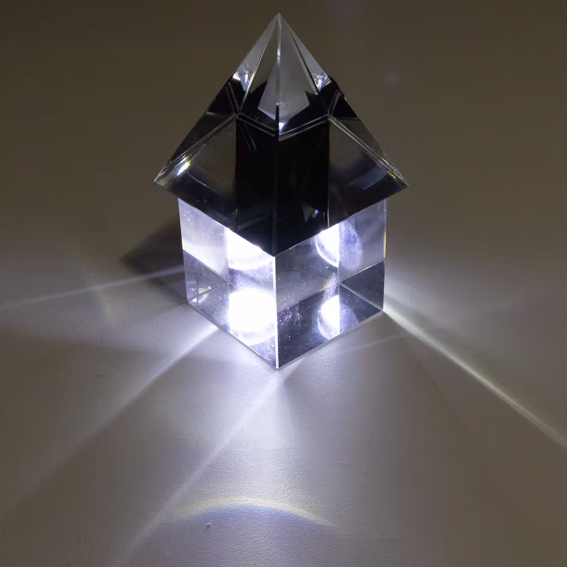Glass pyramid on top of glass cube, with a light shining behind and through them.